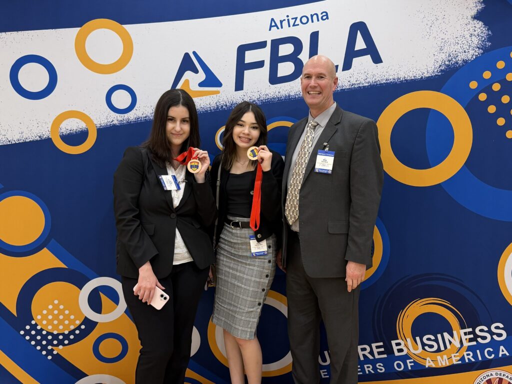 Two students and an advisor pose with medals in front of an Arizona FBLA event backdrop.
